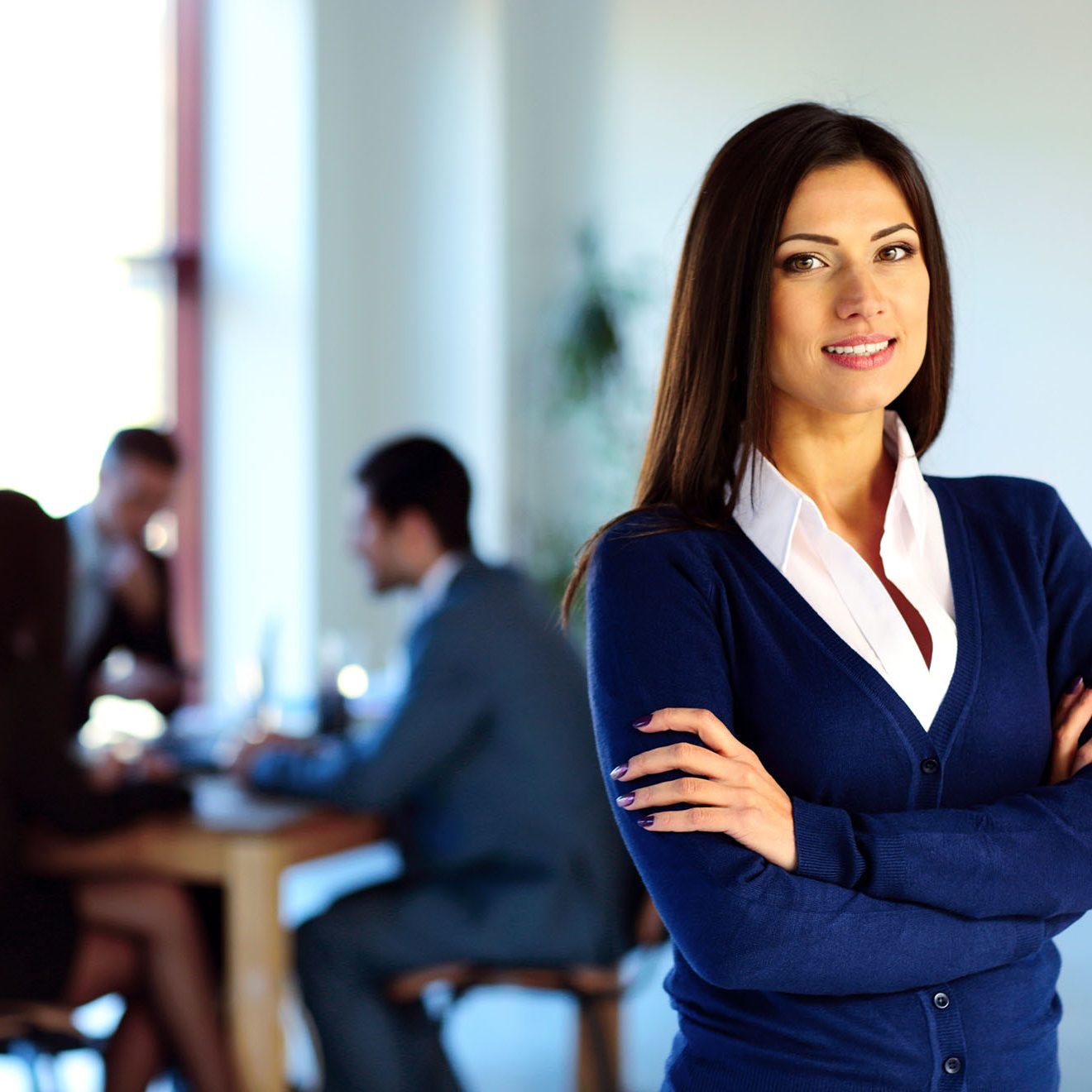 Smiling businesswoman standing with arms folded in front of colleagues Smiling businesswoman standing with arms folded in front of colleagues